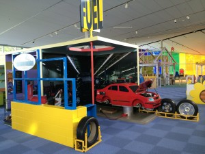 Mechanic exhibit showing a car with its hood up, a yellow wall and tires on display