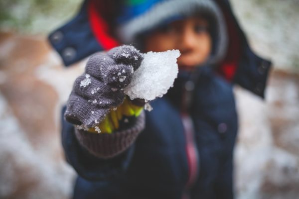 Close up image of a child wearing grey gloves holding a small chunk of snow