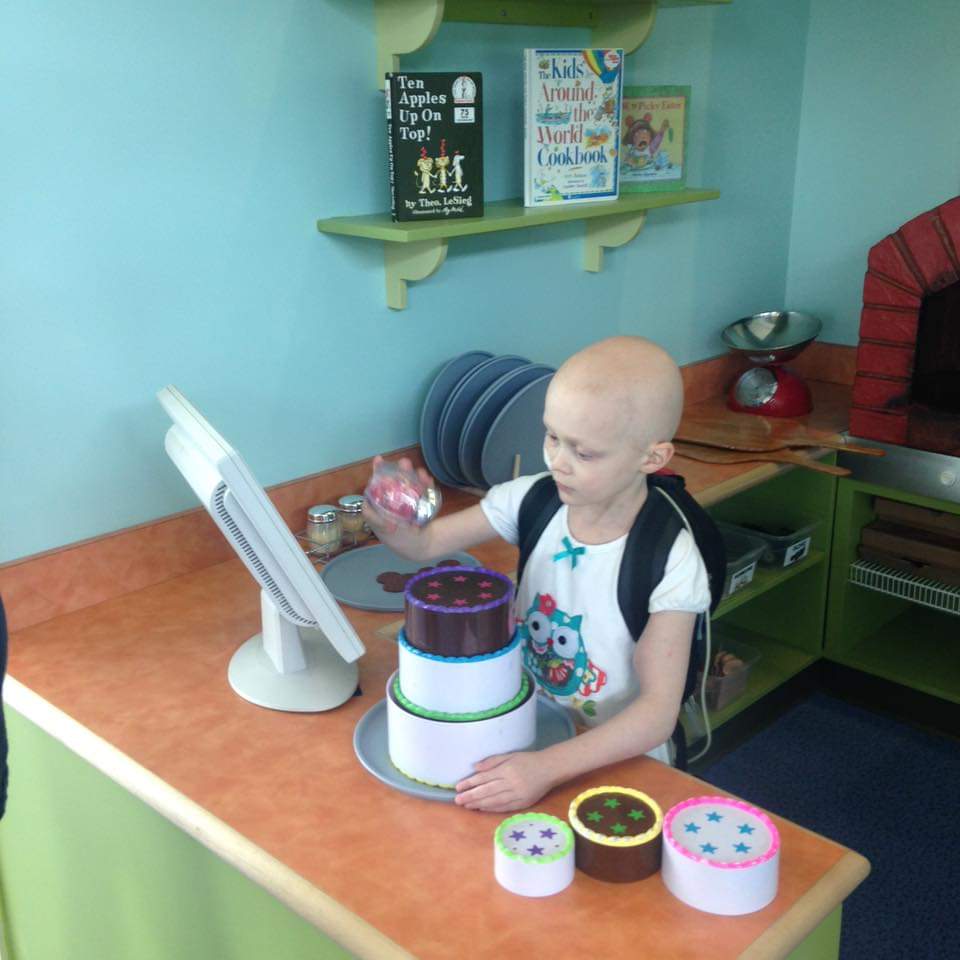A child with no hair due to a medical condition plays with a pretend cake in the cafe exhibit
