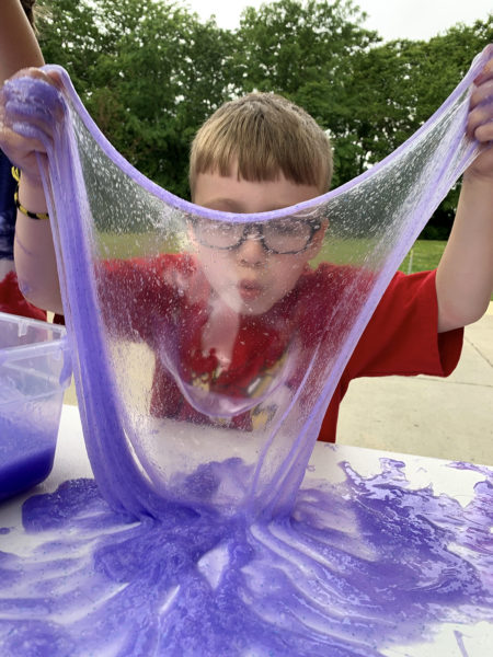 Child in a red shirt blows a bubble in purple slime
